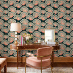 May include: A curved wooden desk with a lamp, a vase of flowers, and a mirror, positioned against wallpaper featuring a repeating pattern of pink peacocks on a dark teal background. A pink upholstered chair with fringe sits in front of the desk.